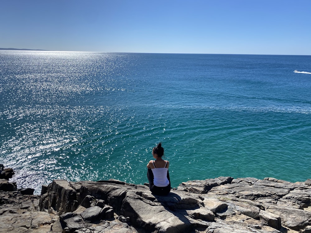 Une femme assise sur des rochers regardant l’océan