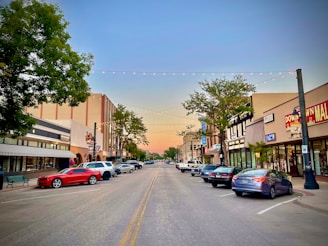 A warm photo of a small town main street at sunset, with people chatting and storefronts glowing.