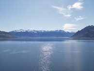 A clear blue lake reflecting the surrounding mountains under a bright sky.
