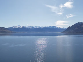 A calm ocean reflecting snow-capped mountains under a clear blue sky.