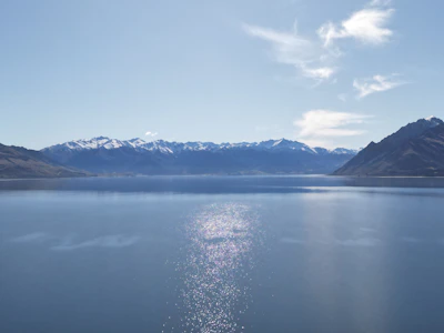 Snow-capped mountains reflecting in a crystal clear lake under a bright, sunny sky.