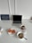 A clean white desk features a closed laptop, a motivational sign on the left, and a breakfast setting. The breakfast includes two slices of bread with salmon on a plate, a bowl of granola with seeds and nuts, a cup of tea with lemon in a red mug, and a pill organizer. The sign reads 'Everyone you meet is fighting a battle you know nothing about. Be kind. Always.'