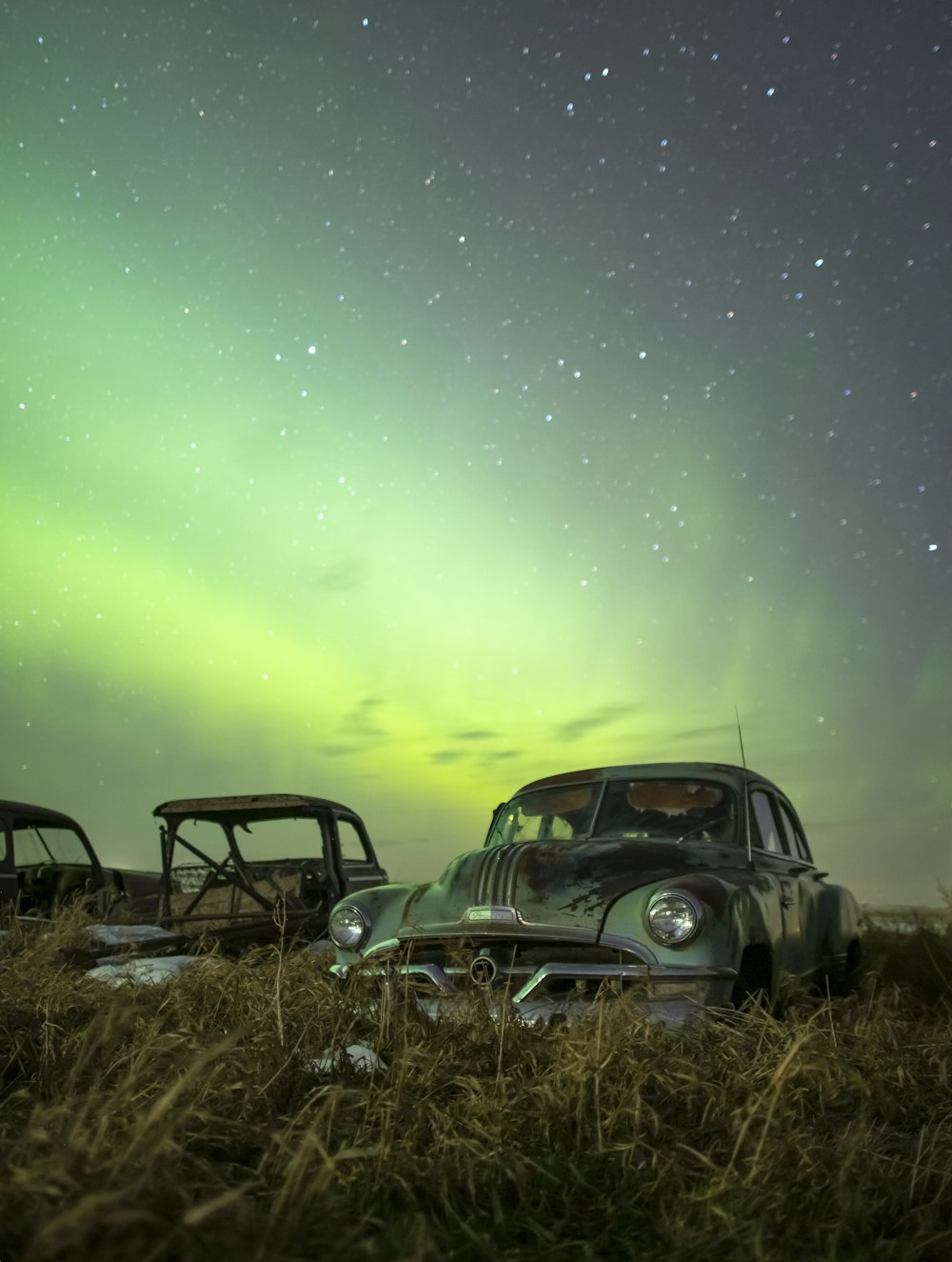 two old cars sitting in a field with the aurora in the background