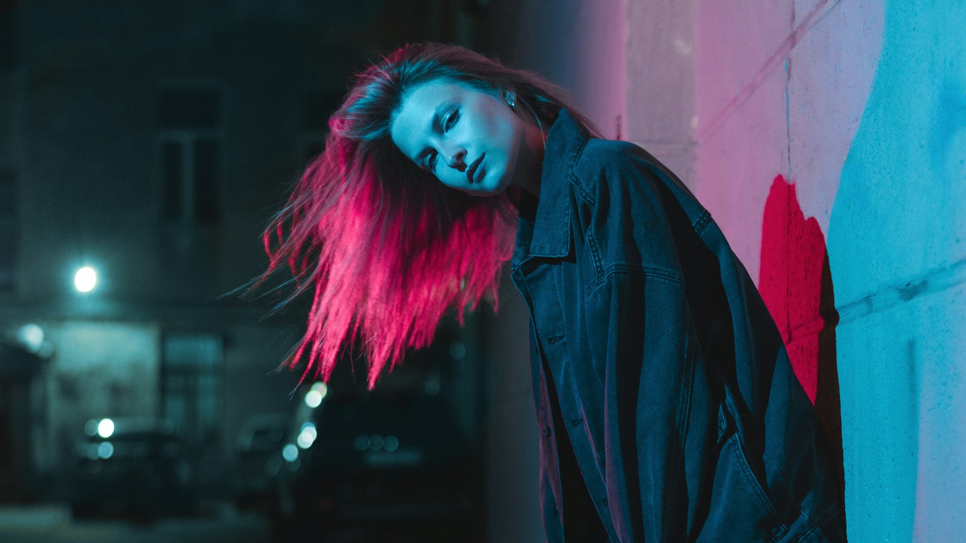 a woman with pink hair leaning against a wall