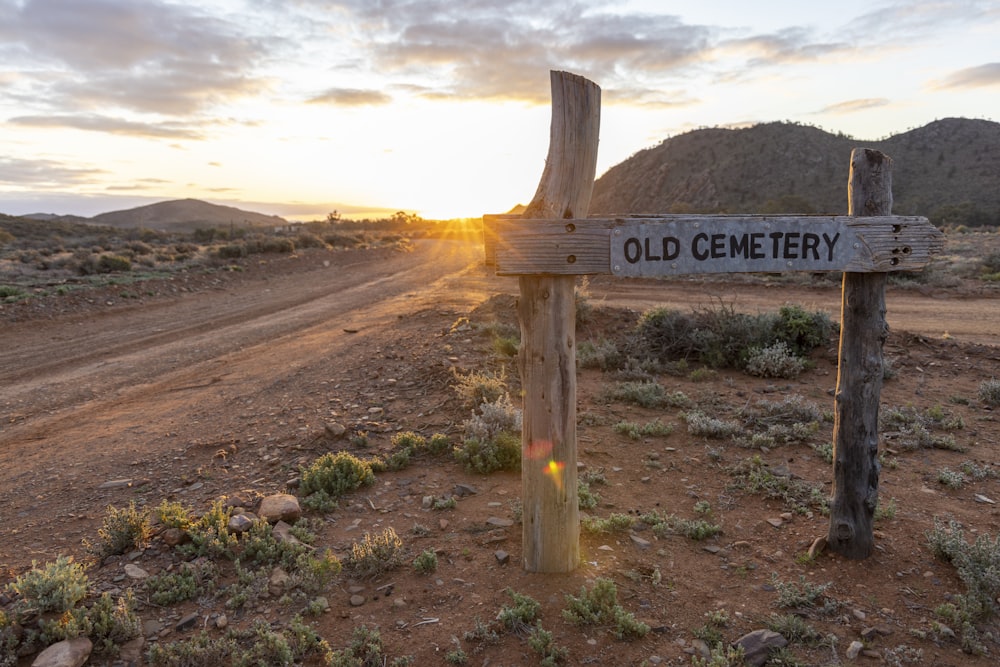 a wooden sign sitting on the side of a dirt road