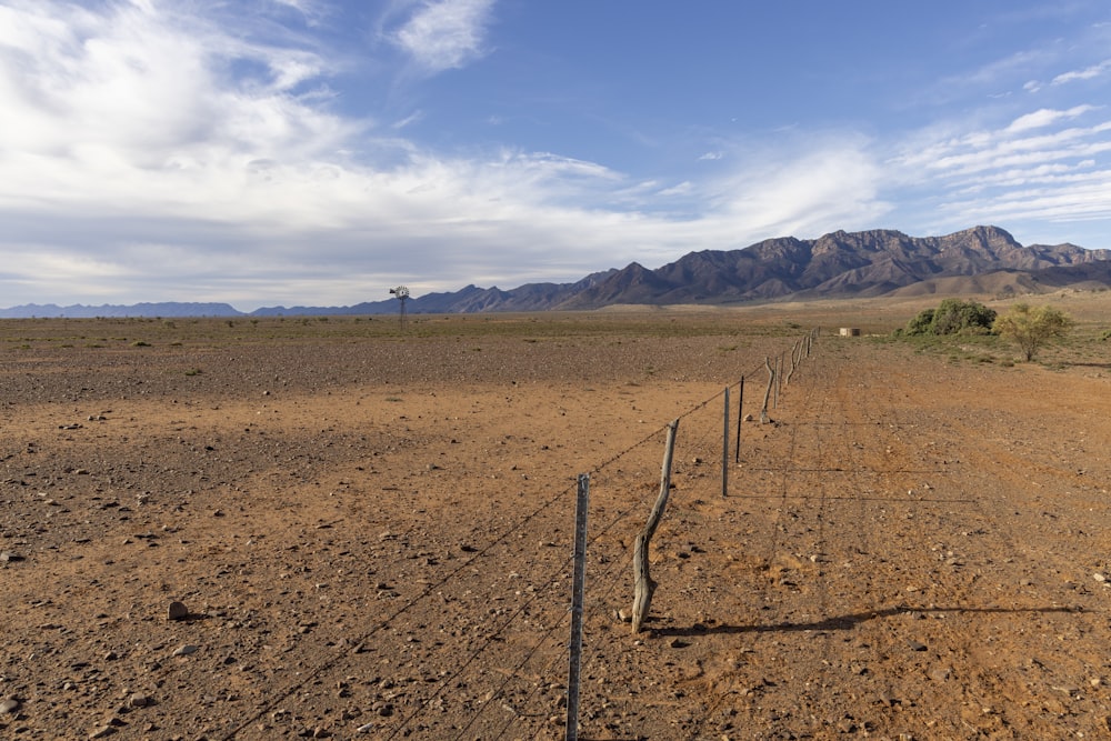a fence in the middle of a desert with mountains in the background