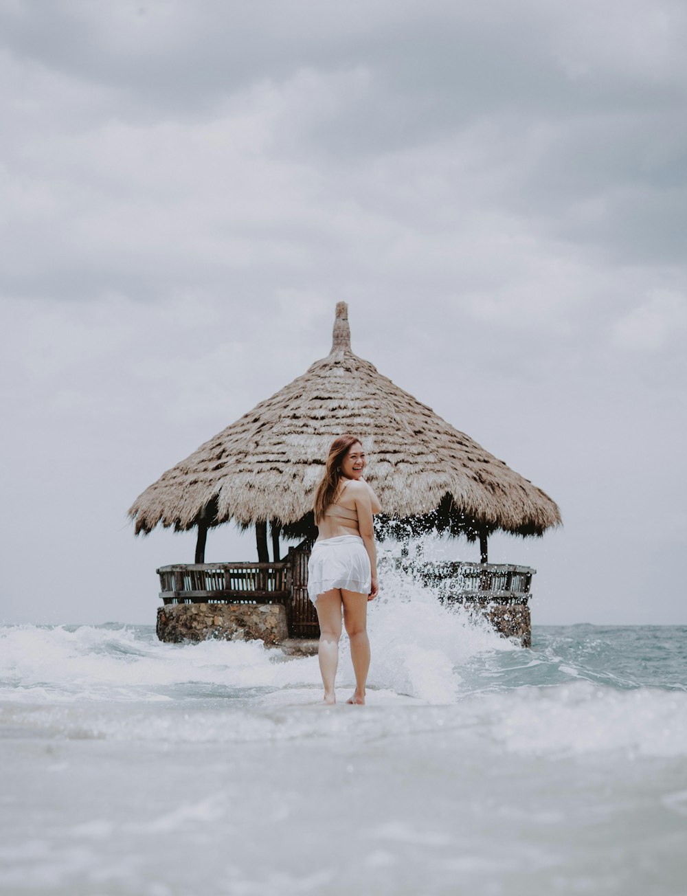 a woman standing in the ocean next to a hut