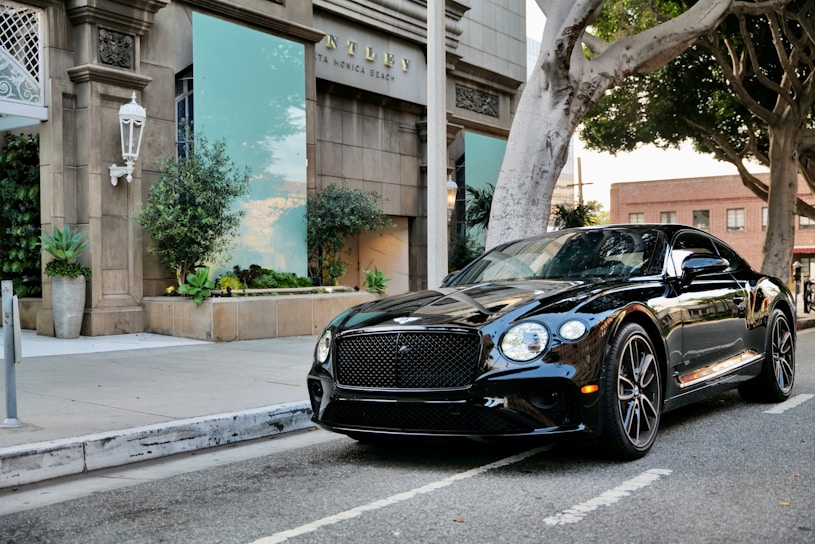 A sleek black luxury car parked on a quiet Lausanne street at dusk, reflecting city lights.