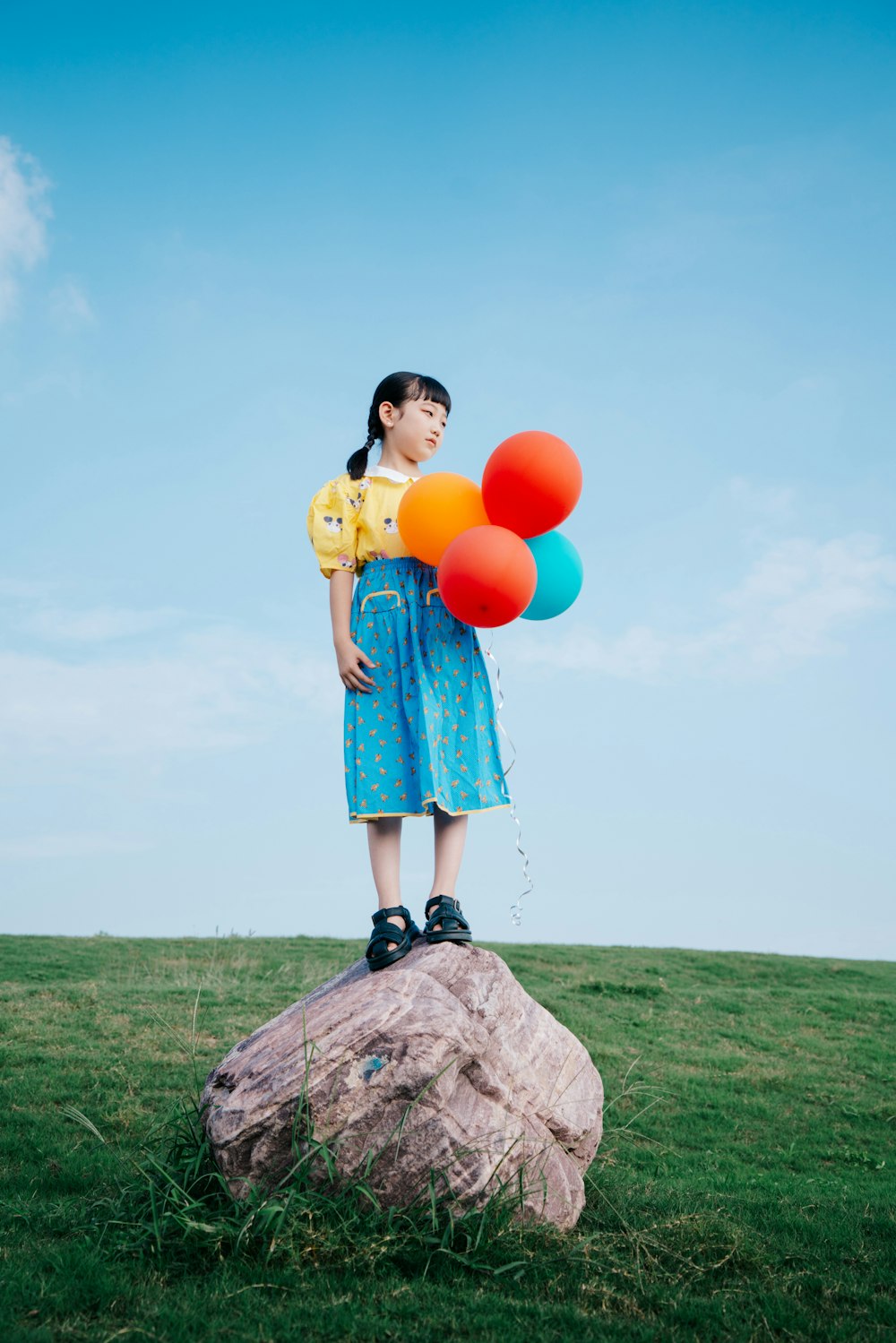 a woman standing on top of a rock holding balloons