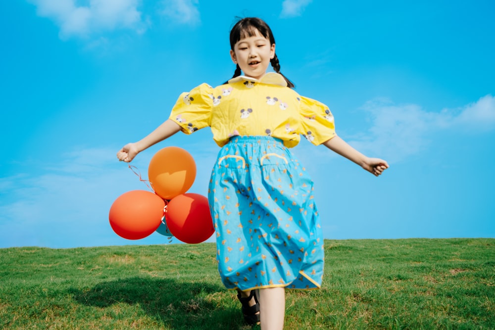a girl in a yellow shirt and blue skirt holding balloons