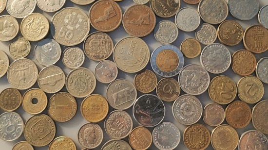 A collection of various coins from different countries and time periods scattered on a flat surface, displaying a range of sizes, designs, and inscriptions.