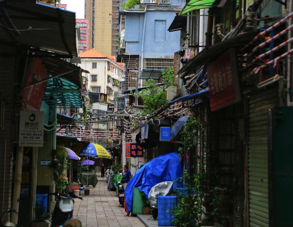 a narrow city street lined with buildings and umbrellas