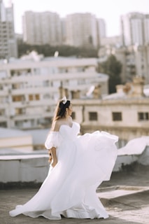 Flowing ivory dress with subtle draping, styled with classic black heels on a city rooftop at dusk