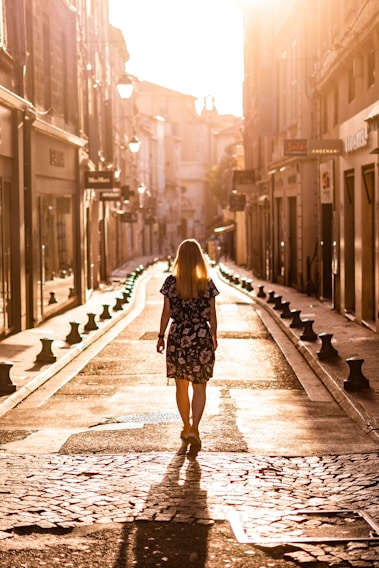 A sunlit city street scene featuring a model wearing a flowing rose gold dress from Lumina Apparel.