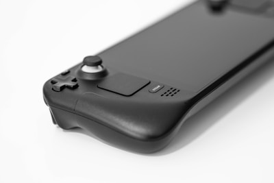 A sleek, modern handheld gaming device with a large screen. It has a black matte finish, featuring a joystick, a D-pad, and several buttons, including one labeled 'Steam'. The design is ergonomic, emphasizing a minimalist and contemporary aesthetic.