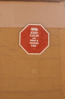 A red octagonal sign mounted on a tan-colored wall with the text 'KEEP CALM AND RENT A WICKED VAN' in white letters along with a white icon of a van at the top.
