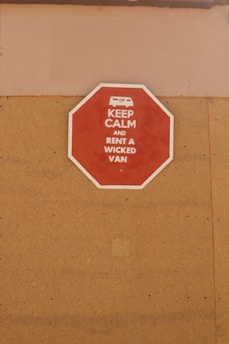 A red octagonal sign mounted on a tan-colored wall with the text 'KEEP CALM AND RENT A WICKED VAN' in white letters along with a white icon of a van at the top.
