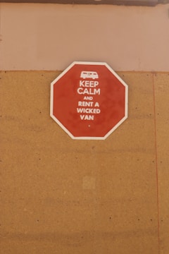 A red octagonal sign mounted on a tan-colored wall with the text 'KEEP CALM AND RENT A WICKED VAN' in white letters along with a white icon of a van at the top.