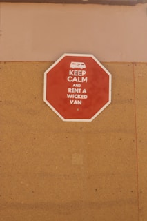 A red octagonal sign mounted on a tan-colored wall with the text 'KEEP CALM AND RENT A WICKED VAN' in white letters along with a white icon of a van at the top.