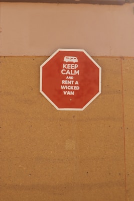 A red octagonal sign mounted on a tan-colored wall with the text 'KEEP CALM AND RENT A WICKED VAN' in white letters along with a white icon of a van at the top.