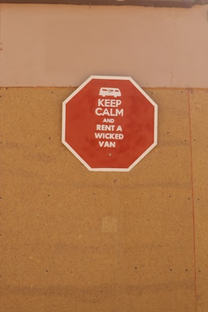A red octagonal sign mounted on a tan-colored wall with the text 'KEEP CALM AND RENT A WICKED VAN' in white letters along with a white icon of a van at the top.