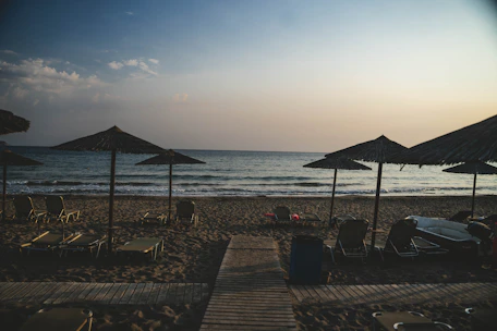 A serene beach setup with sun loungers and umbrellas overlooking the calm Mediterranean sea at sunset.