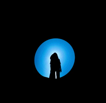 Silhouetted figure standing against a glowing cyan neon circle backdrop.