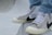 A close-up of a person's feet wearing high-top sneakers. The sneakers are a collaboration between Off-White and Nike, featuring a beige and white color scheme with black detailing and text on the side. The shoes rest on a smooth, curved concrete surface, possibly part of a skate park. The person is dressed in light blue jeans.
