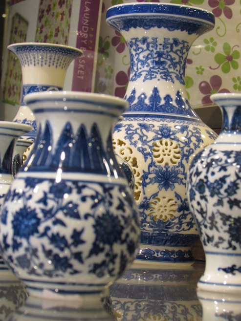 A collection of intricately designed blue and white porcelain vases, featuring floral and geometric patterns. The vases are displayed closely together on a reflective surface, enhancing their elegance and craftsmanship.