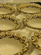A collection of ornately designed ceramic or porcelain bowls with an elegant floral pattern featuring gold and white colors. The bowls are resting on a soft, white fabric, enhancing their luxurious appearance.