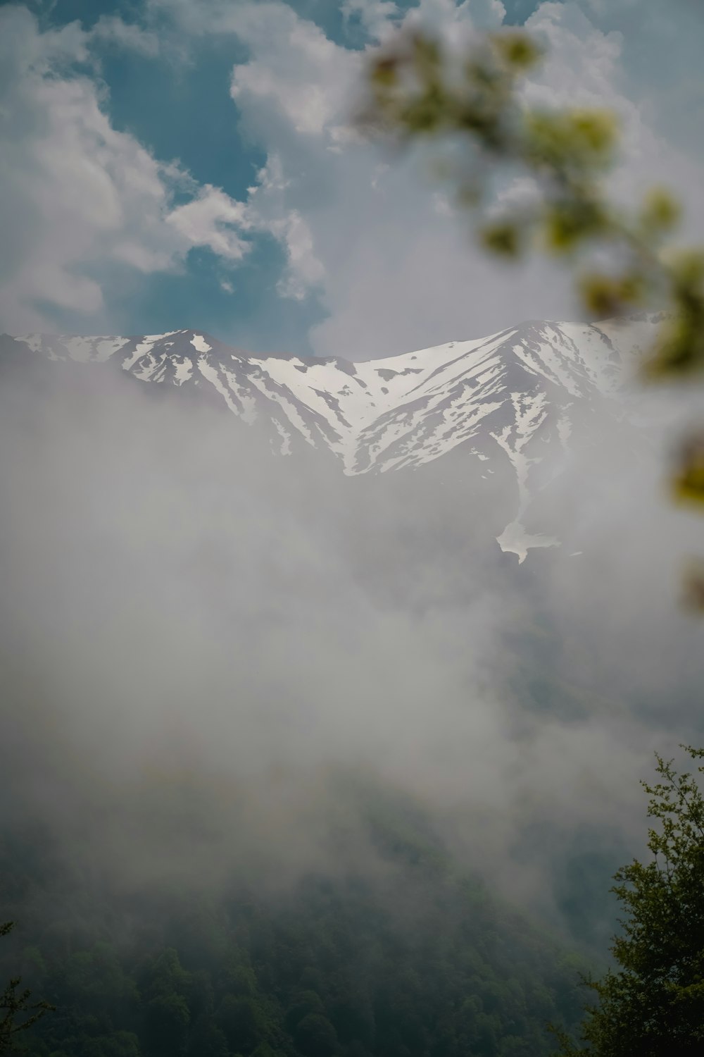 a mountain covered in snow and clouds under a blue sky