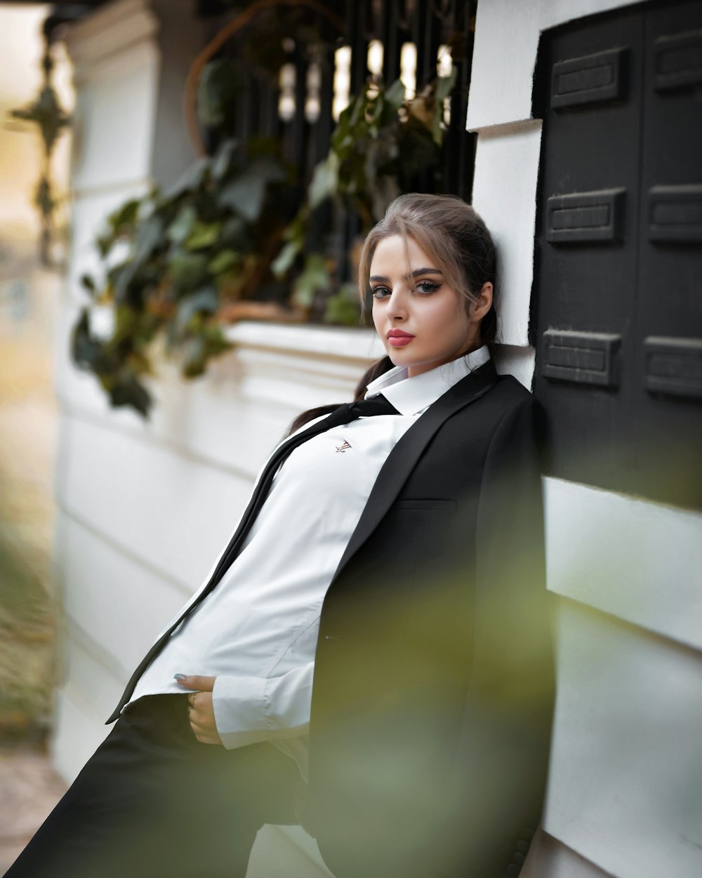 a woman in a suit leaning against a wall