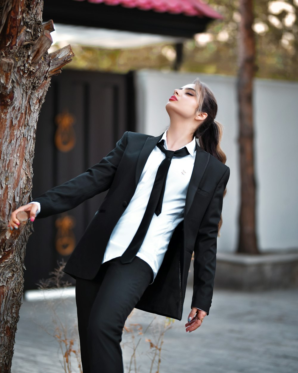 a woman in a suit leaning against a tree