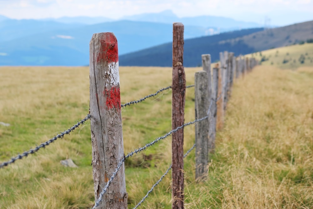 a wooden fence in a grassy field with mountains in the background