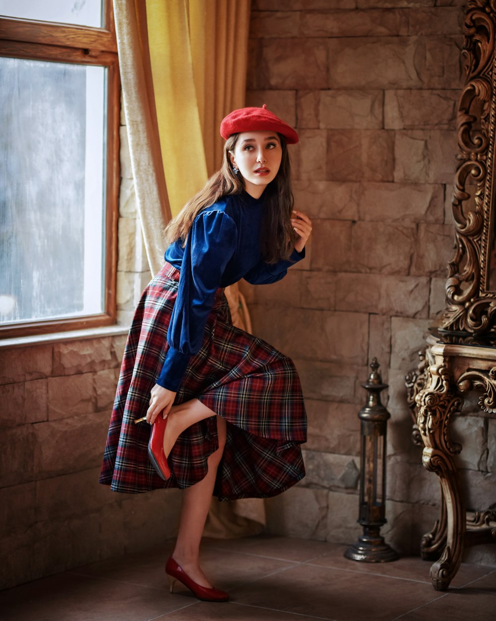 Una mujer con un vestido azul y sombrero rojo posando frente a una ventana