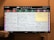 The image depicts a television screen displaying a Japanese TV guide with multiple channels and time slots. Various programs are listed with text in Japanese. Below the TV, two white mugs with a hotel name logo are placed on a surface.