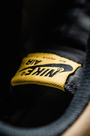 A close-up view of a yellow fabric label with the word 'Nike' and the swoosh logo, stitched onto a black surface. The texture of the fabric and stitching details are clearly visible.