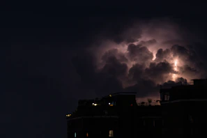 Dark clouds swirling above shattered skyscrapers with sparks of electrical fires.