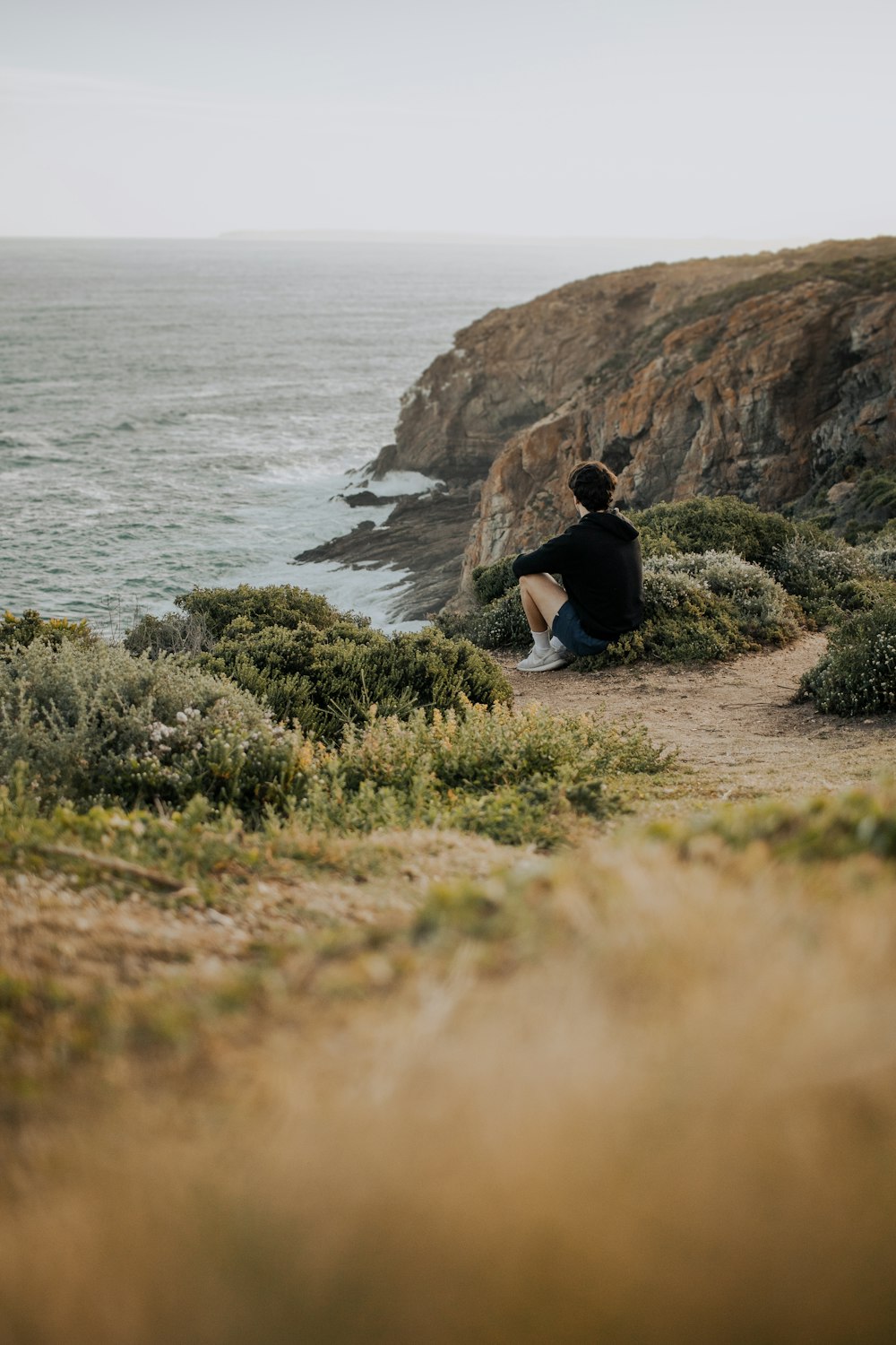 a man sitting on a cliff overlooking the ocean