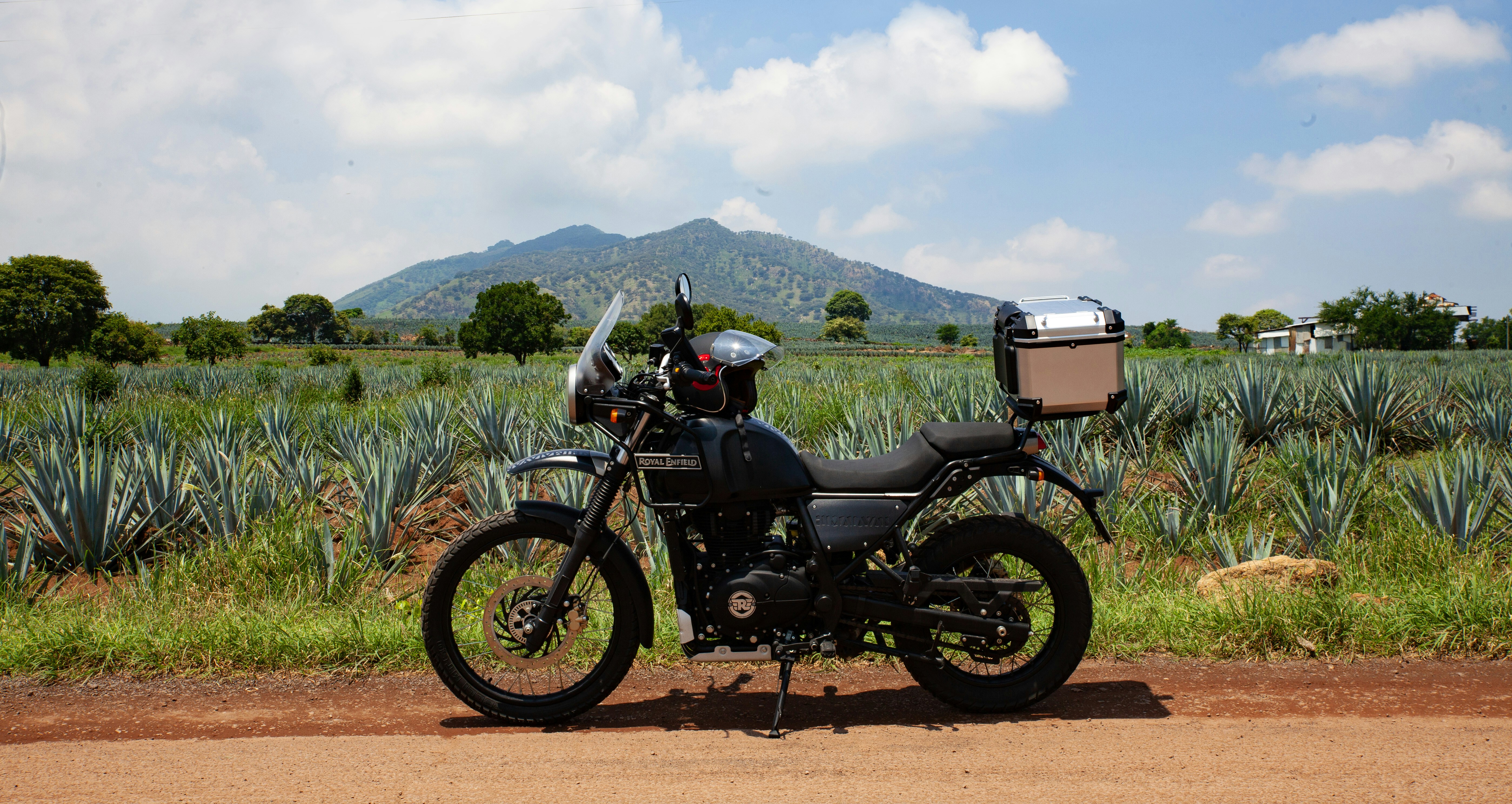 a motorcycle parked on the side of a dirt road, 