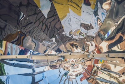 A complex structure made of metallic panels arranged in a radial pattern, creating reflections and distortions of surrounding objects and colors. The metallic surfaces are shiny and the panels are bolted together.