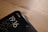 A close-up view of the top corner of a smartphone, displaying the time 19:16, the day SAT, and the date 20/10. The phone screen shows two network providers, Jio and BSNL, in the top right corner. The phone is placed on a wooden surface, with a smooth and slightly reflective finish.