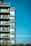 A modern apartment building with multiple floors featuring glass balconies and large windows against a clear blue sky.