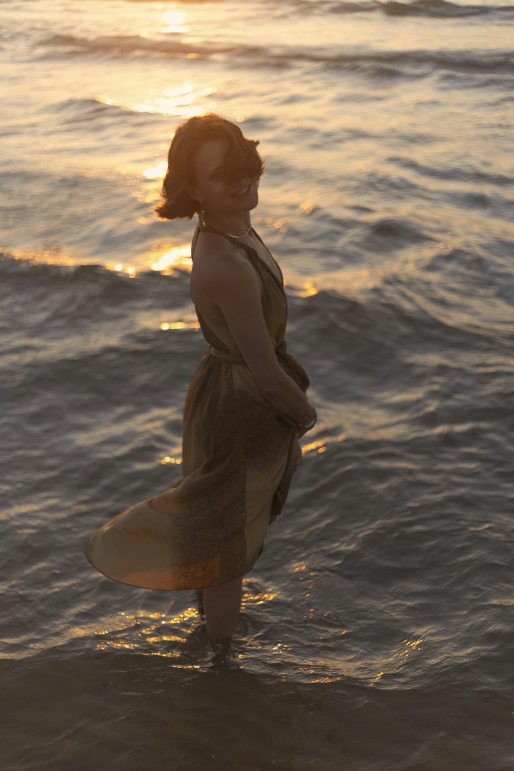 a woman standing in the ocean at sunset