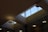 A geometric ceiling with large rectangular skylights allowing natural light to illuminate the space. The structure includes modern light fixtures and glass partitions.
