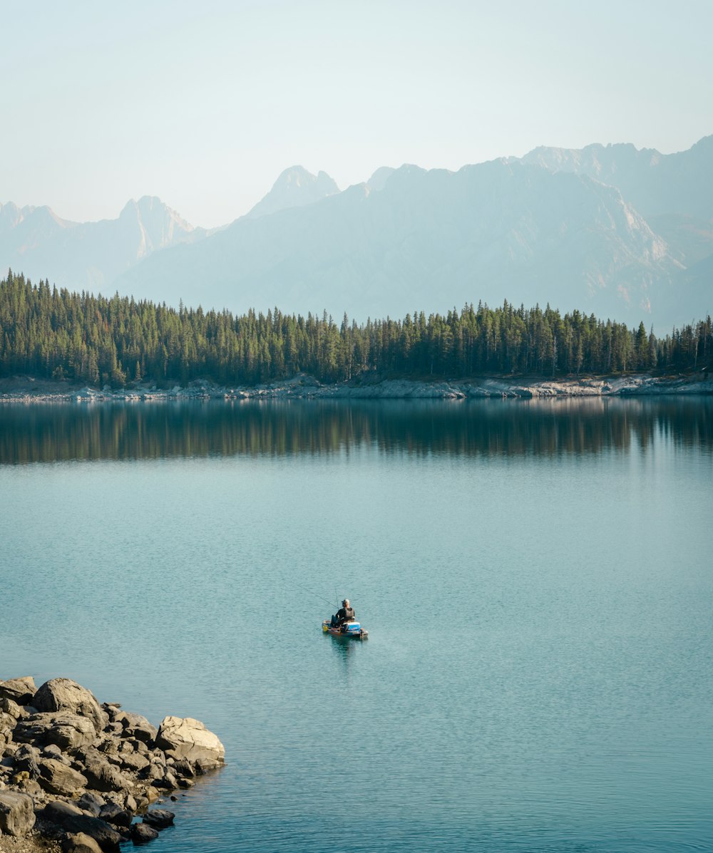 a person in a boat on a lake with mountains in the background