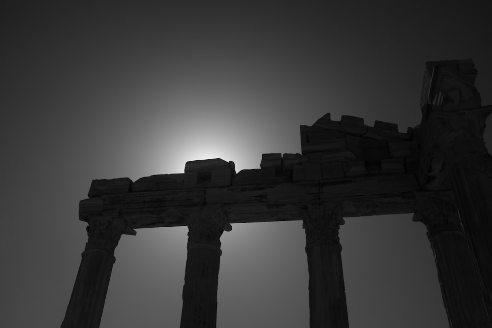 a black and white photo of the sun behind some pillars