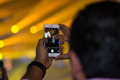 A person happily recording a video using a smartphone with a bright background.