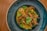 A beautifully plated dish of seafood consisting of crab legs and shrimp, garnished with fresh basil leaves. The ingredients are placed on a bed of creamy sauce, within a deep blue ceramic dish, set against a wooden table backdrop.