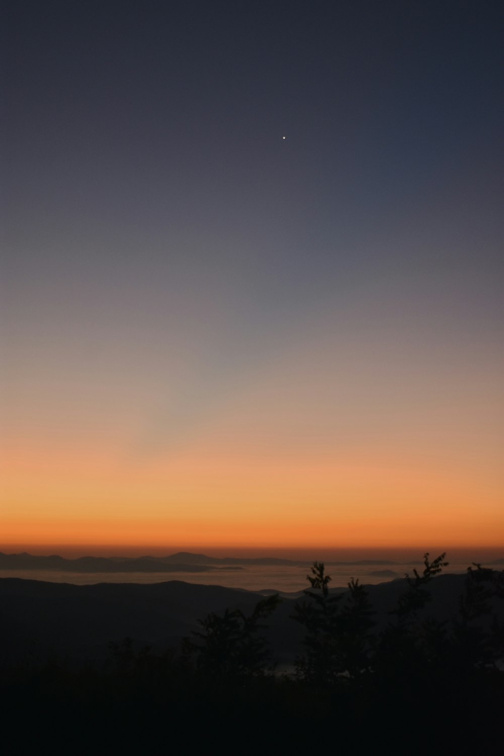 the sun is setting over the horizon of a mountain range